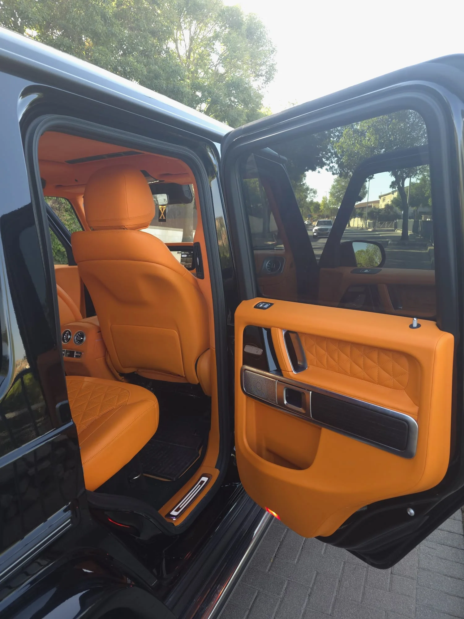 The rear door of a black Mercedes-AMG G63 open, with orange leather door trim and seats inside