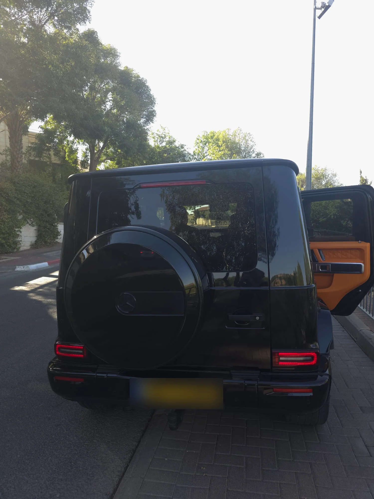 מרצדס G63 שחורה מאחור, עם כיסוי הגלגל הרזרבי השחור והדלת האחורית פתוחה לפנים כתום